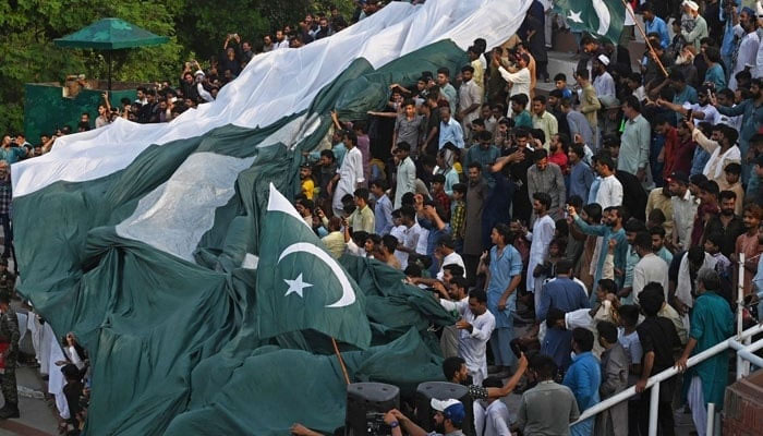 People carry a giant Pakistan flag while watching Beating the Retreatceremony on the eve of country’s Independence Day celebrations at the Pakistan-India Wagah border post near Lahore. — AFP/File