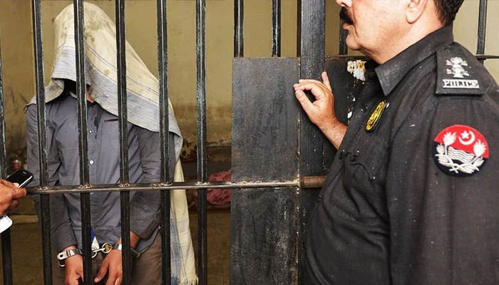 A handcuffed suspect stands behind the bars with a policeman standing outside the cell in this undated image. — AFP/File