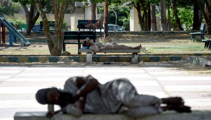 Men sleep on benches under the shade of trees at a park on a hot summer afternoon in Karachi on May 24, 2024. — AFP