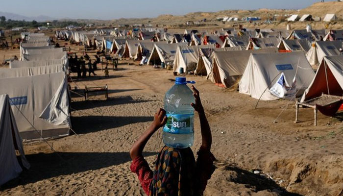 A displaced girl carries a bottle of water she filled from nearby stranded flood-waters, as her family takes refuge in a camp, in Sehwan on September 30, 2022. — Reuters