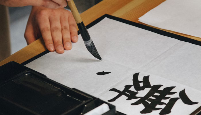 This representational image shows a person writing Japanese words. — Unsplash/File