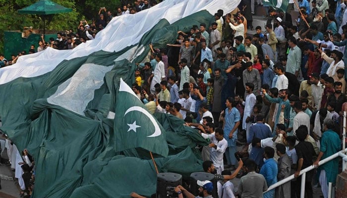 People carry a giant Pakistan flag while watching Beating the Retreatceremony on the eve of country’s Independence Day celebrations at the Pakistan-India Wagah border post near Lahore. — AFP/File