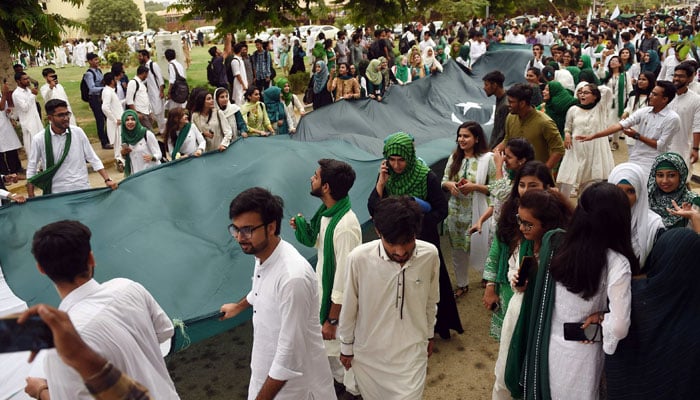 A representational image showing University of Karachi students carrying a large national flag as part of the Independence Day celebrations. — AFP/File