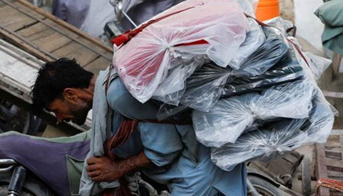 A labourer bends over as he carries packs of textile fabric on his back to deliver to a nearby shop in a market in Karachi on June 24, 2022. — Reuters