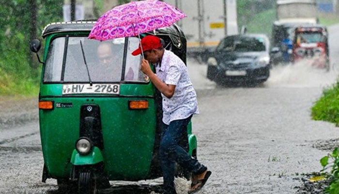 A man walking though rain with an umbrella as a riskhaw approaches behind him.— AFP/File