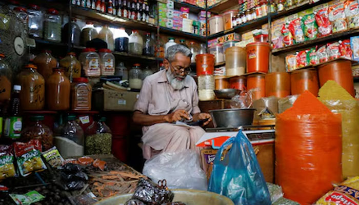 A shopkeeper uses a calculator while selling spices and grocery items along a shop in Karachi. — Reuters/File