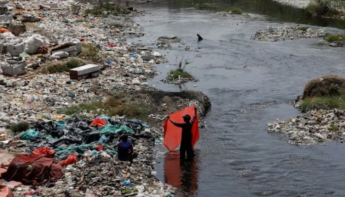 A man washes waste plastic sheets, collected for recycling, in the polluted waters on World Environment Day in Karachi on June 5, 2023. —Reuters