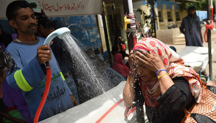 A volunteer showers a woman with water during a heatwave in Karachi. — AFP/File