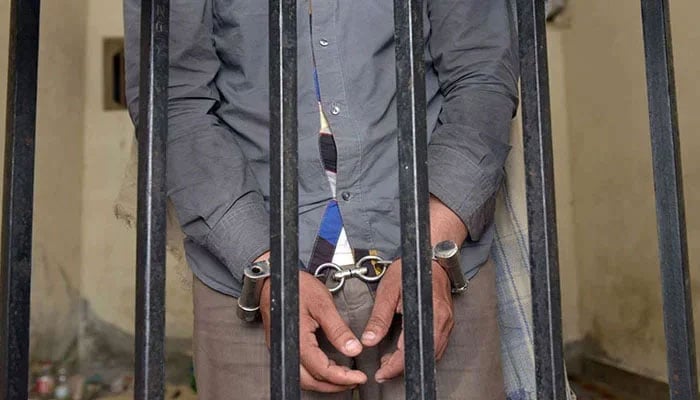 A representational image showing a person handcuffed behind bars. — AFP/File