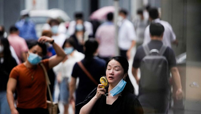 A woman wearing face mask uses a fan as she walks on a street on a hot day in Shanghai, China on July 19, 2022. — Reuters