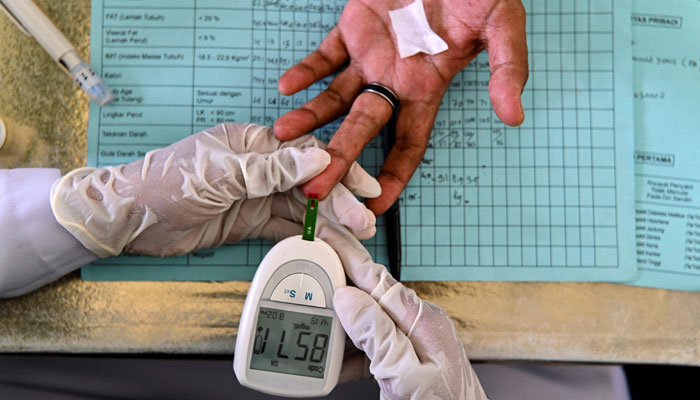 An elderly woman gets her blood tested during a drive to provide medical check-ups for hypertension, cholesterol and diabetes at an integrated services post in Banda Aceh on December 15, 2021. — AFP