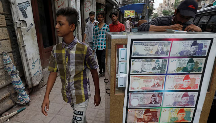 A boy walks past a sidewalk money exchange stall decorated with pictures of banknotes in Karachi on September 30, 2021. — Reuters