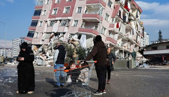 Children sit in a shopping cart near a collapsed building following an earthquake in Hatay, Turkey, February 7, 2023. — Reuters