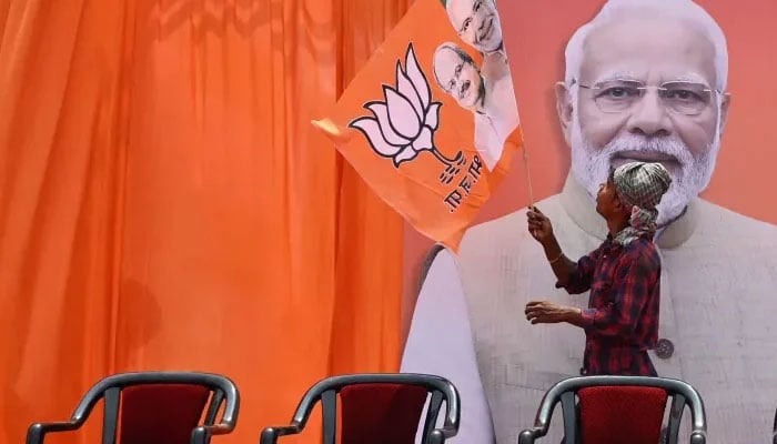 A worker fixes a flag of the ruling Bharatiya Janata Party on a hoarding of their leader and India’s Prime Minister Narendra Modi on April 15, 2024. — AFP