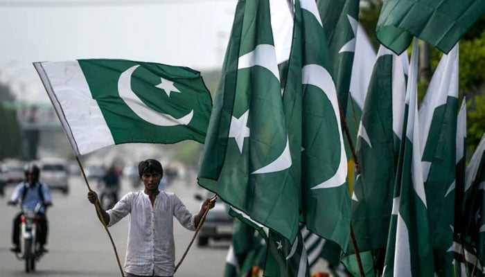 A vendor holds a Pakistani flag as he waits for customers beside his stall alongside a street in Islamabad on August 13, 2020. — AFP