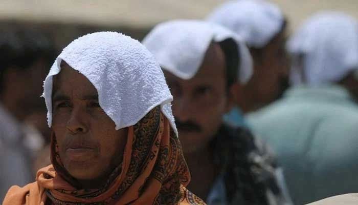 People cover their heads covered with wet towels as they wait outside a hospital during a heatwave in Karachi. — AFP/File
