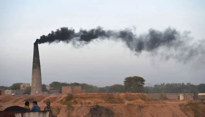 This picture shows smoke billowing from a chimney as Pakistani labourers rest beside a brick kiln. — AFP/File