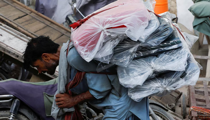 A labourer bends over as he carries packs of textile fabric on his back to deliver to a nearby shop in a market in Karachi on June 24, 2022. — Reuters