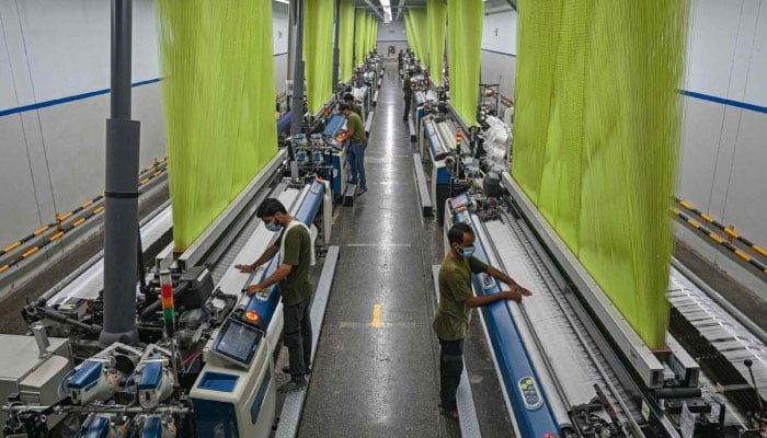 Workers operate machines preparing fabric at a textile mill in Lahore on July 20, 2023. — AFP