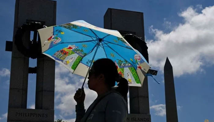 A visitor shields herself from the sun with an umbrella at the World War II Memorial amid a heat wave in Washington DC, Jun 19, 2024. — Reuters