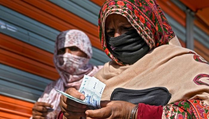 In this file photo, a woman in a face mask counts rupee notes as she walks on a street in Islamabad on April 9, 2020. — AFP