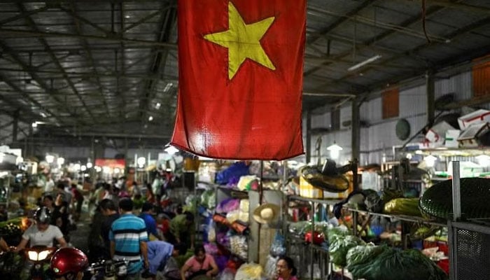 The Vietnamese flag is seen as vegetable vendors wait for customers at a wholesale market in Hanoi, Vietnam. — AFP