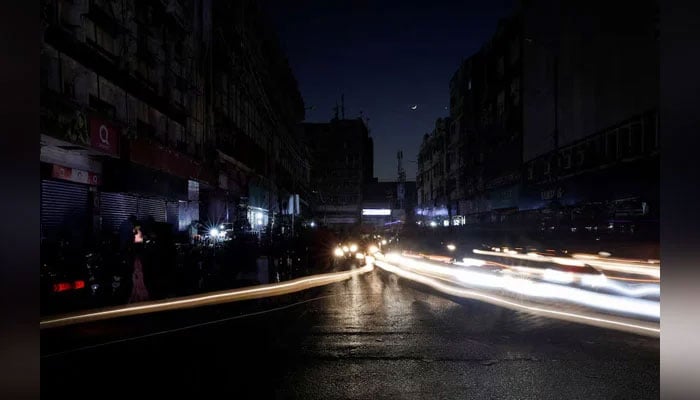 Vehicle lights cause light streaks on the road along a market, during power outages in Pakistan. — Reuters/File