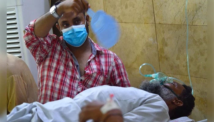 An attendant waves a handheld fan over a patient who is receiving treatment at the heatstroke emergency ward of a hospital in Karachi, Pakistan on June 25, 2024. — INP