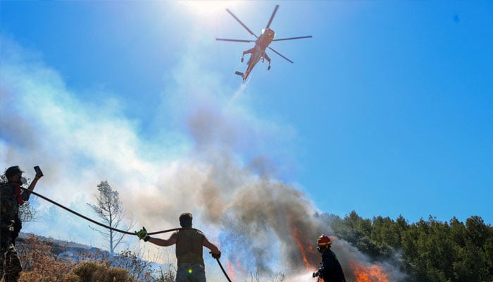 A firefighting helicopter flies over a firefighter and volunteers trying to extinguish a wildfire burning in Keratea, near Athens, Greece, June 30, 2024. — Reuters