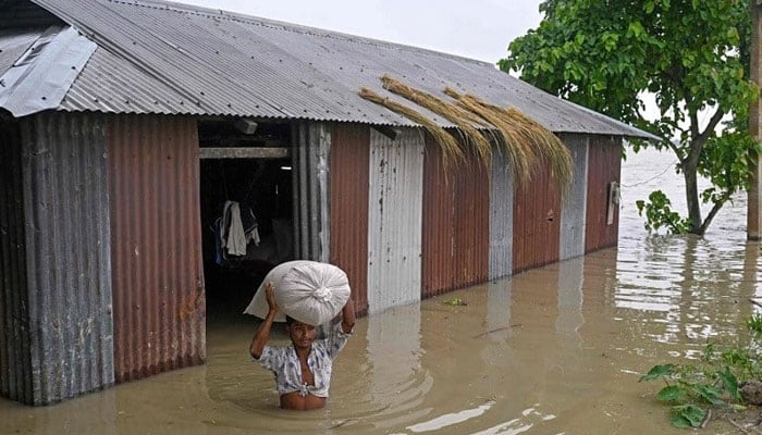 A man wades through floodwaters as he carries a sack of rice from his house deluged by heavy rain in Morigaon district in Assam, India. — AFP/File