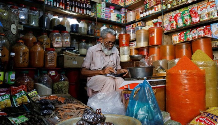A representational image showing a shopkeeper uses a calculator while selling spices and grocery items along a shop in Karachi. — Reuters/File