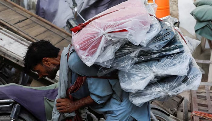 A labourer bends over as he carries packs of textile fabric on his back to deliver to a nearby shop in a market in Karachi on June 24, 2022. — Reuters