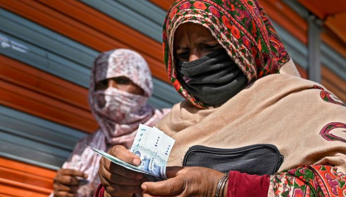 In this file photo, a woman in a face mask counts rupee notes as she walks on a street on April 9, 2020. — AFP