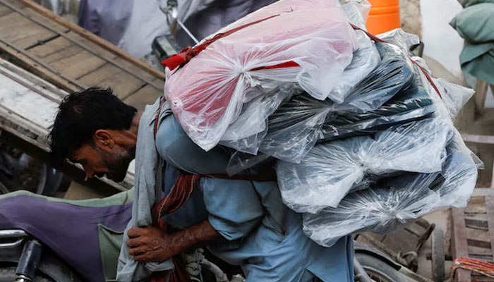 A labourer bends over as he carries packs of textile fabric on his back to deliver to a nearby shop in a market in Karachi, Pakistan June 24, 2022. — Reuters