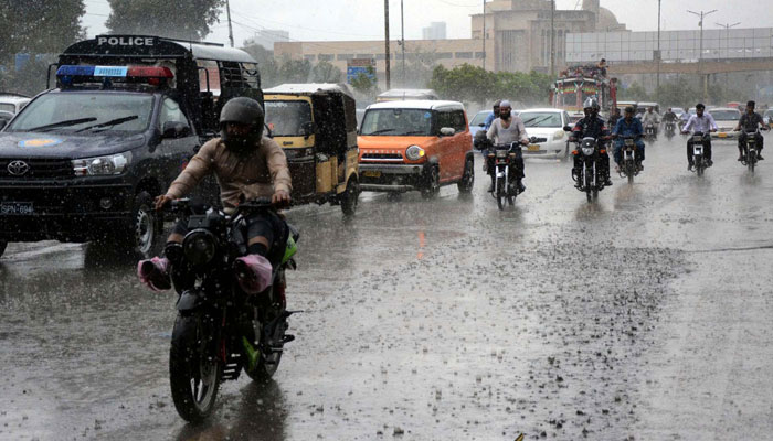 Commuters pass through a road during heavy downpour of monsoon season, at Shahrah-e-Faisal road in Karachi on July 9, 2024. — PPI