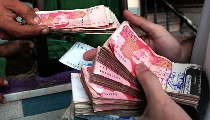 Two persons can be seen holding notes of Pakistani currency Rupee in their hands. — AFP/file