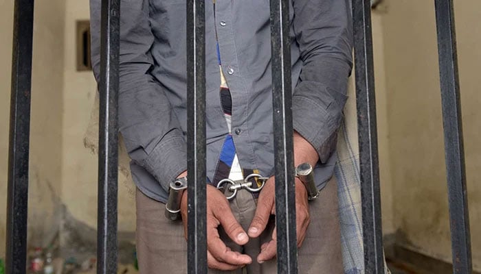 A representational image showing a person handcuffed behind bars. — AFP/File