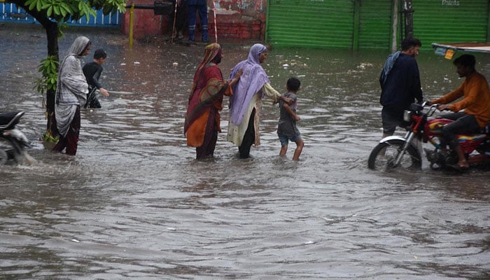 People passing through accumulated water on the road during rain in Lahore on July 12, 2024. — APP