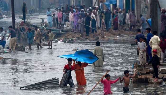 People wade through a flooded residential area after heavy monsoon rains in Pakistan´s port city of Karachi. — AFP/File