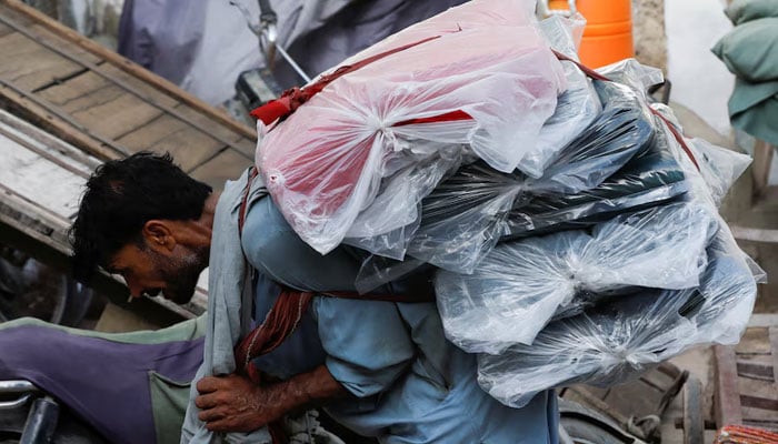 A labourer bends over as he carries packs of textile fabric on his back to deliver to a nearby shop in a market in Karachi, Pakistan June 24, 2022. — Reuters