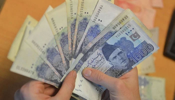 A money changer counts Pakistans currency at a market in Karachi. — AFP/File