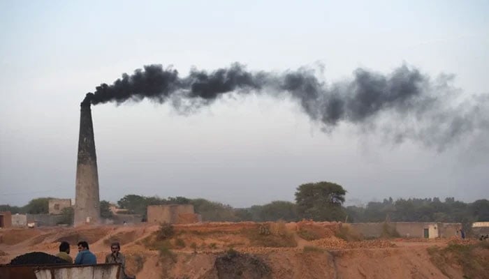 This picture shows smoke billowing from a chimney as Pakistani labourers rest beside a brick kiln on the outskirts of Islamabad. — AFP/File