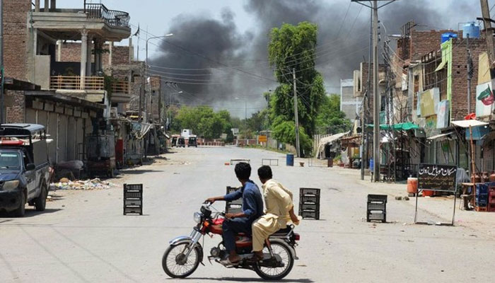 Men riding a bike watch as smoke rises following an explosion allegedly after militants suicide squad attempted to storm an army cantonment that houses military residences and offices in Bannu on July 15, 2024. — AFP