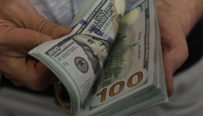 A teller flicks through a bundle of US dollars at an exchange office on July 20, 2023. — AFP