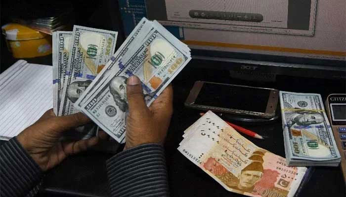 A currency dealer is counting notes of $100 while Rs5,000 notes are placed on the table. — AFP/File