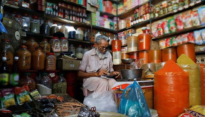 A shopkeeper uses a calculator while selling spices and grocery items along a shop in Karachi, Pakistan June 11, 2021. — Reuters