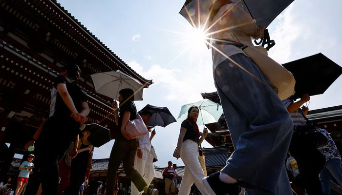 Passers holding umbrellas walk in strong sunlight heat stroke alerts on July 22, 2024 — Reuters