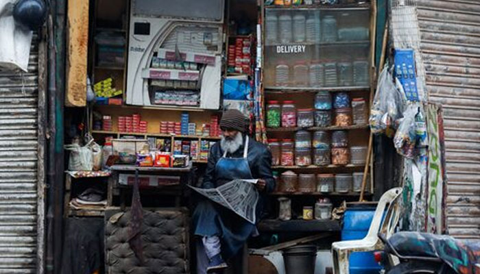 A man reads newspaper while selling betel leaves, known as pan, cigarettes and candies from a shop in Karachi, Pakistan, December 30, 2021. — Reuters