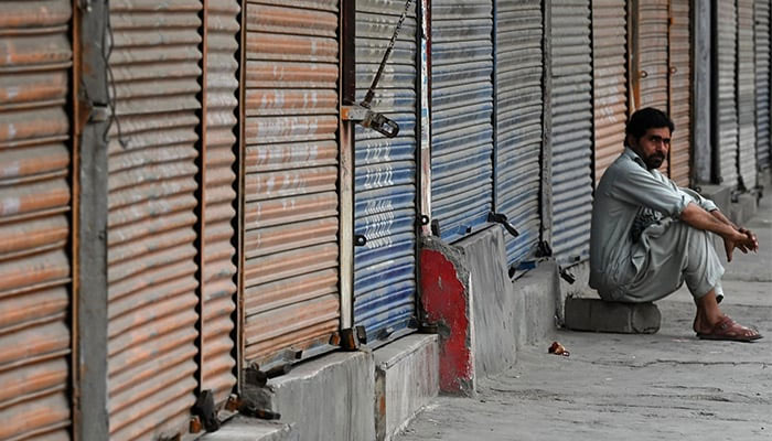 A man sits in front of closed shops along a roadside in Peshawar on September 2, 2023, during a nationwide strike by traders against the surge in electricity and fuel prices. — AFP