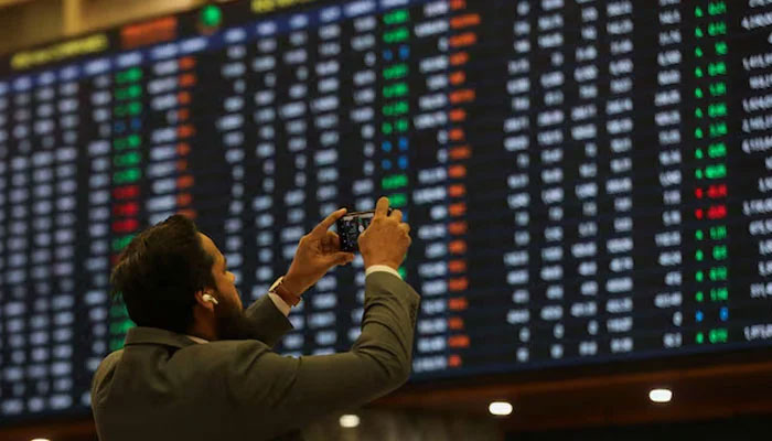 A man uses a mobile phone as he takes a photo of the electronic board displaying share prices during a trading session at the Pakistan Stock Exchange, Karachi, Pakistan November 28, 2023. — Reuters